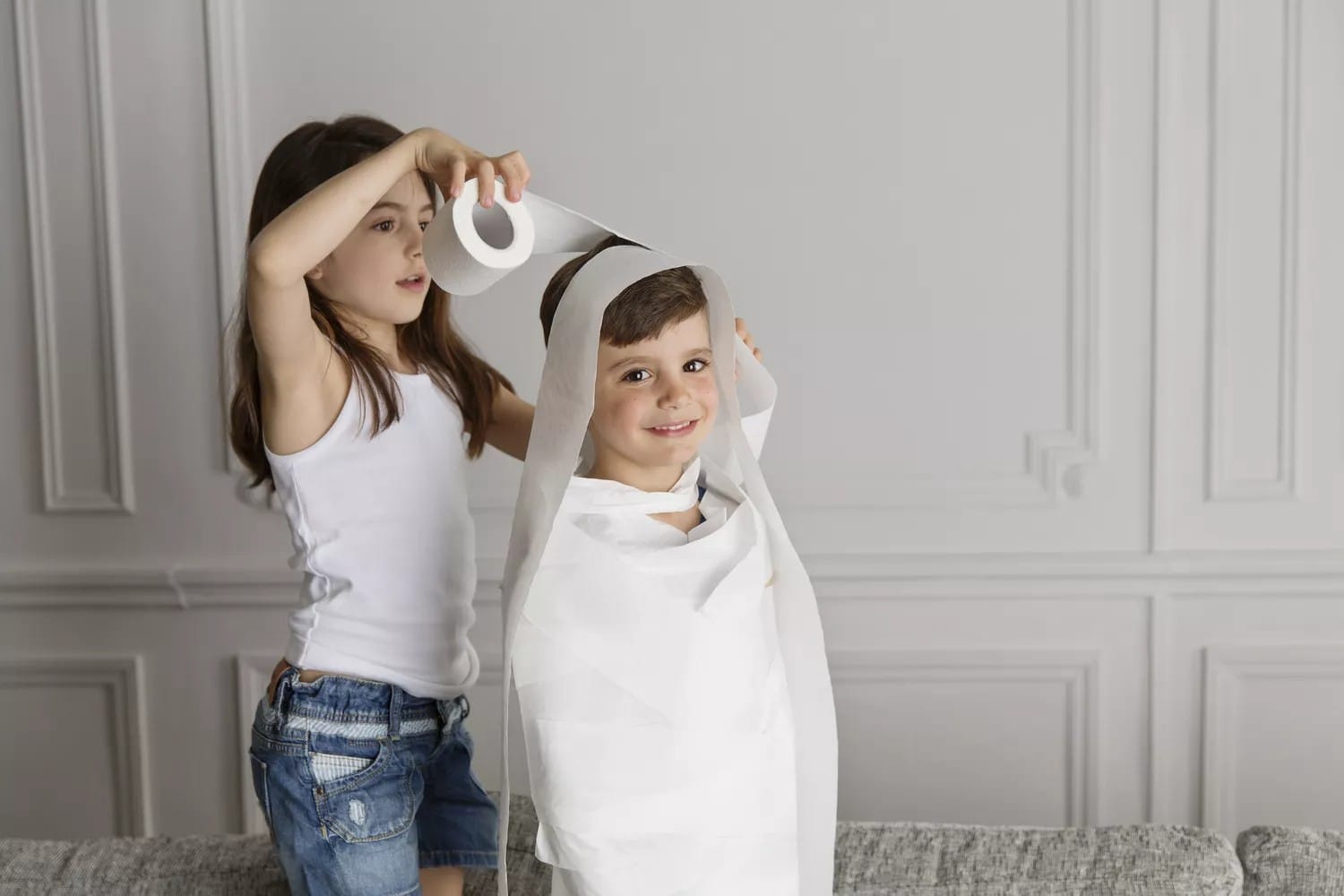 Mummy Wrap girl wrapping toilet paper around her little brother at home
