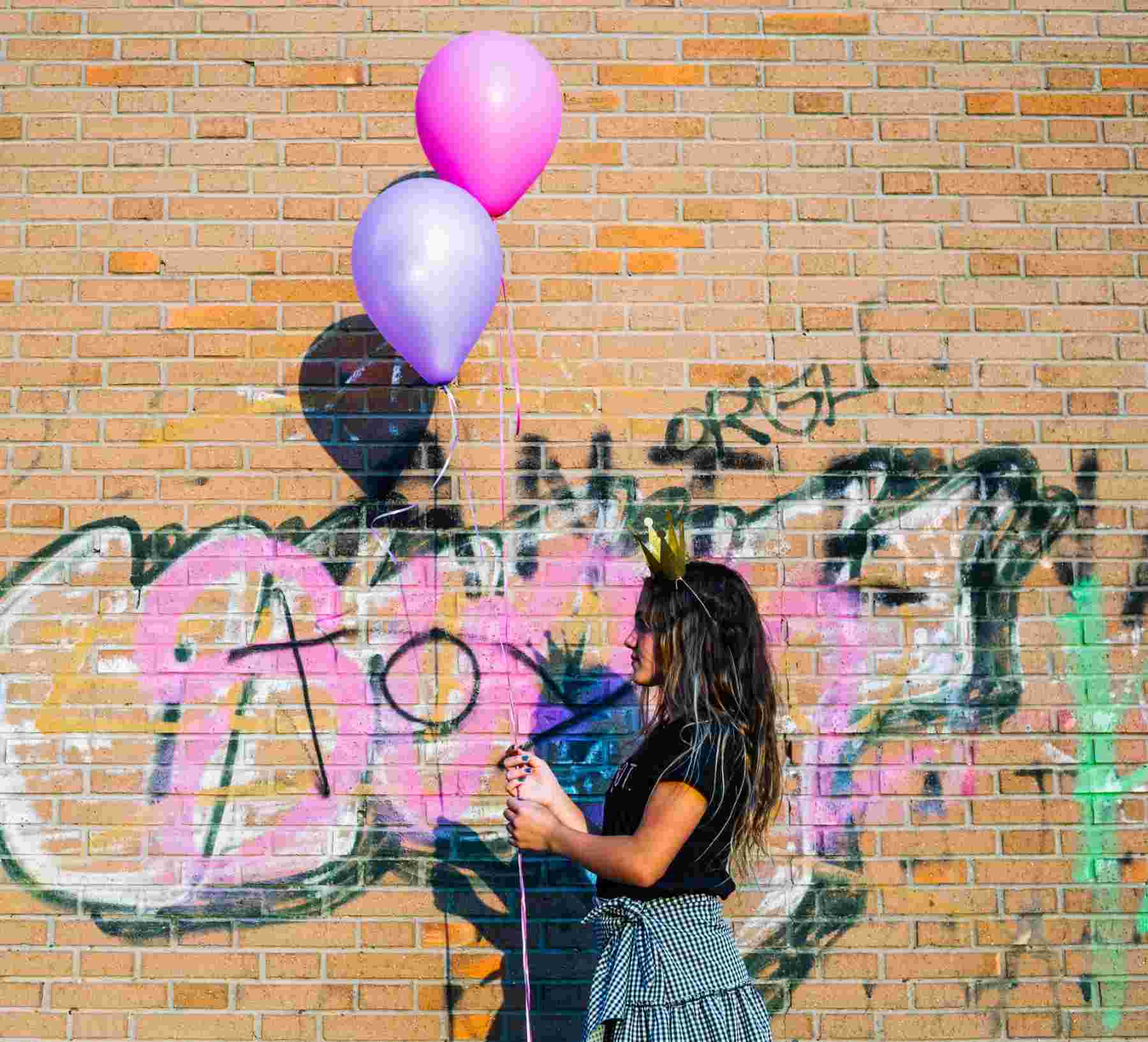 girl party holding balloons front graffiti wall