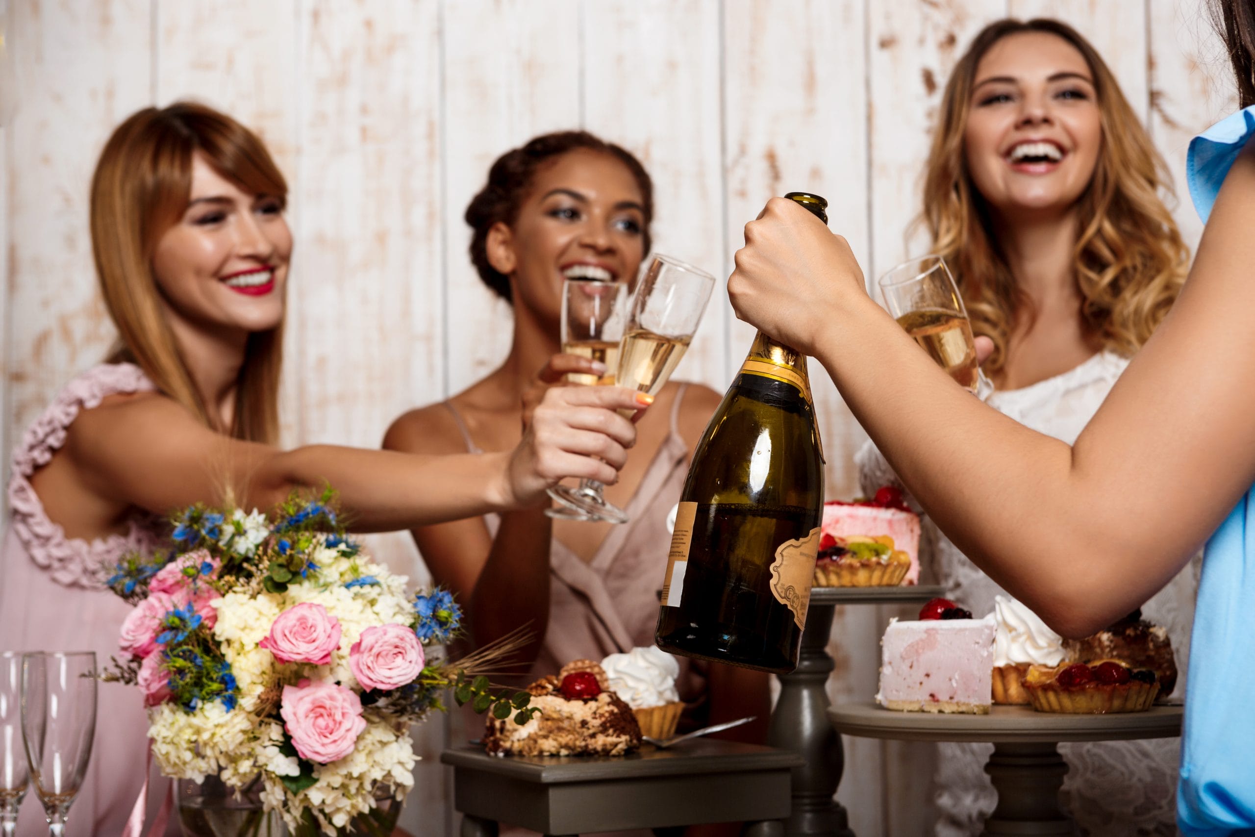 Four young beautiful girls in dresses holding glasses with champagne, speaking, smiling, laughing, resting at party.