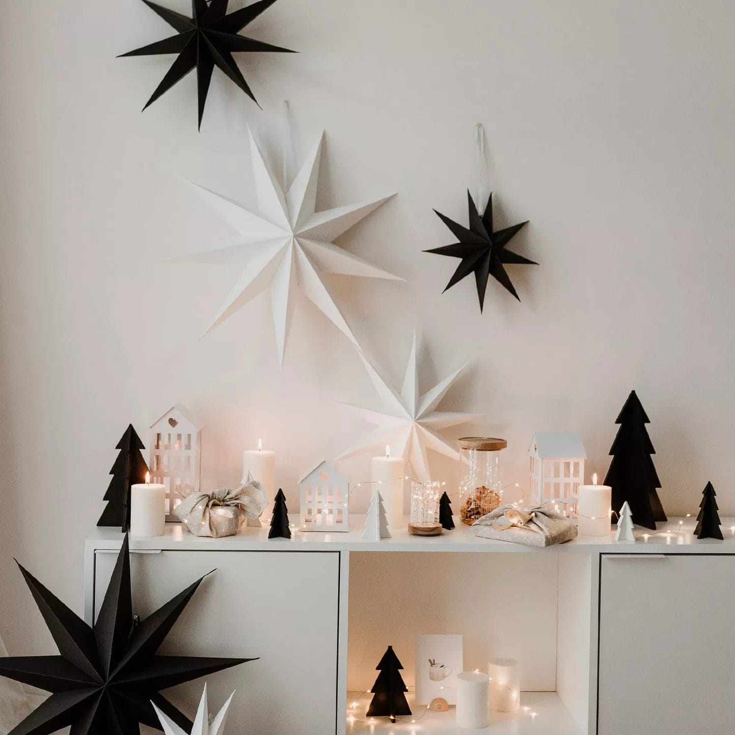 Christmas decoration with black and white paper stars on the wall above an atmospherically decorated sideboard.