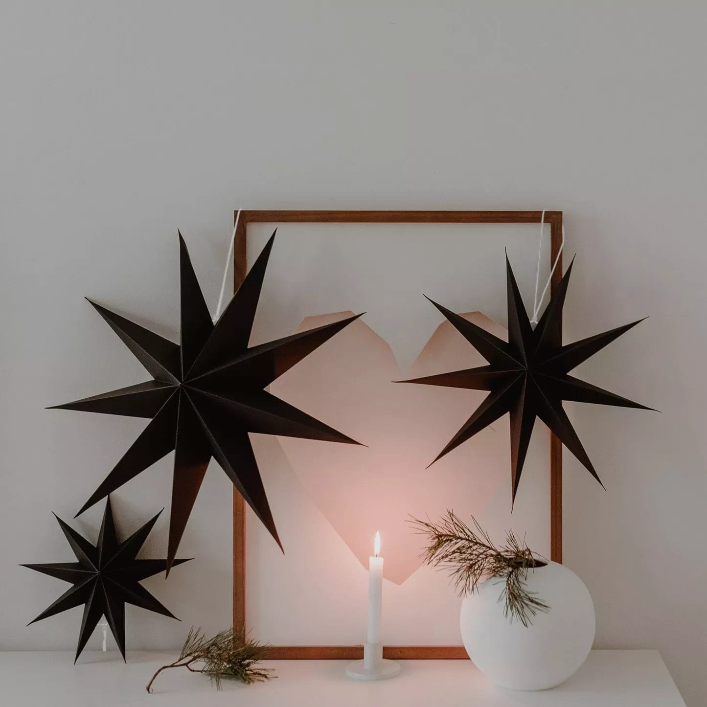 Three black paper stars as wall decorations with candles and picture frames – stylish Christmas atmosphere in the interior.