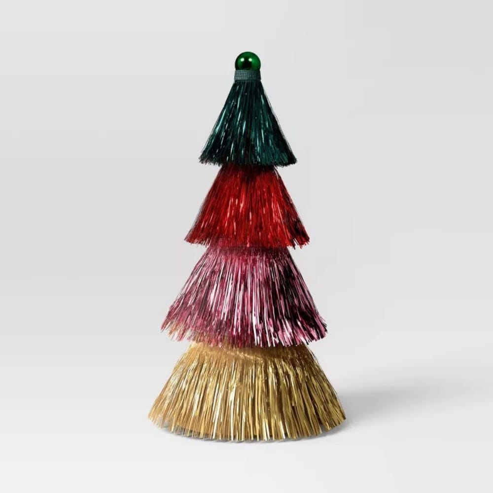 A tiered tinsel tree decoration with layers in green, red, pink, and gold colored tinsel topped with a green colored ornament.