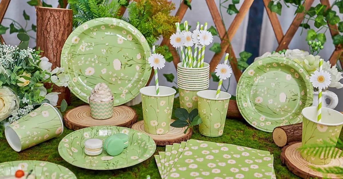 A fresh, nature-inspired collection with green plates, cups, and napkins adorned with delicate white daisies, set against a mossy, woodsy bac